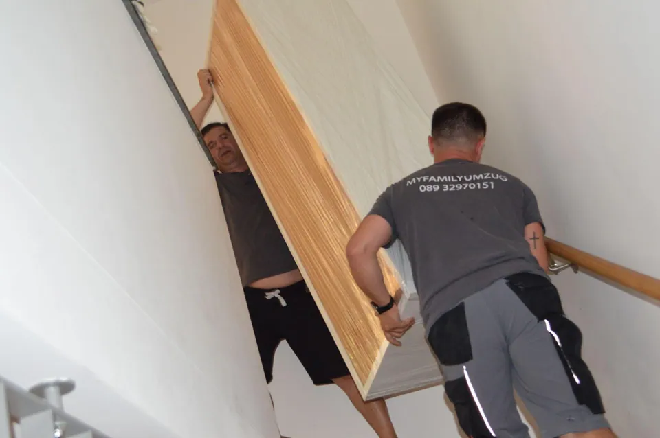 Mitarbeiter tragen ein großes Möbelstück durch ein enges Treppenhaus bei einer Entrümpelung